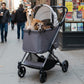 Two dogs in a Ibiyaya Maxi pet stroller on a city street with people walking by.